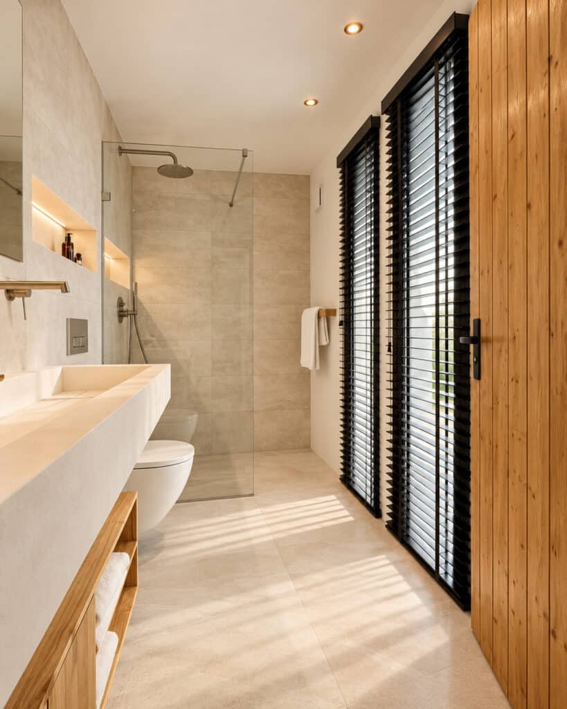 Badkamer met inloopdouche, lichte tegels in natuursteenlook en een houten deur
