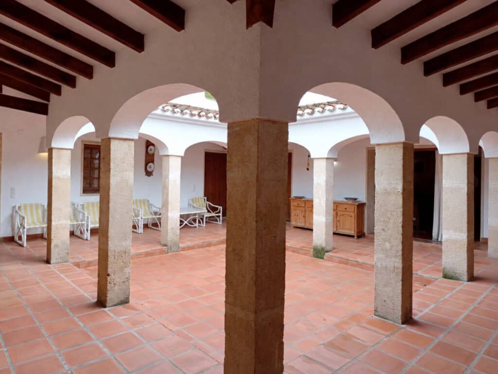 Patio vóór de renovatie, met terracotta vloer, donkere balken en oude tuinmeubels